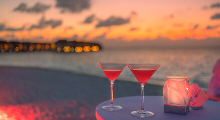 Two cocktail drinks blur beach coast party people and colorful sunset sky in background. Luxury outdoor leisure lifestyle, relaxing and romantic colors, blurred people partying on a summer evening
