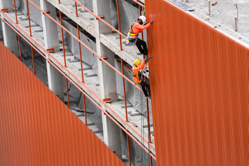 workers install material of metal wall on facade structure building. The construction of modern hi...