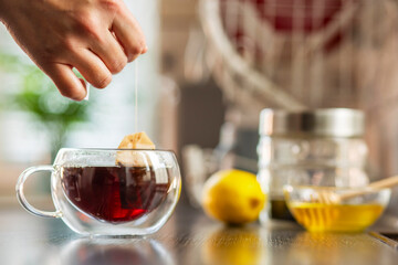 Womans hand puts the tea bag in the glass cup with hot water