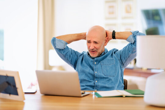 Mid aged man with laptop sitting at home and having web conference