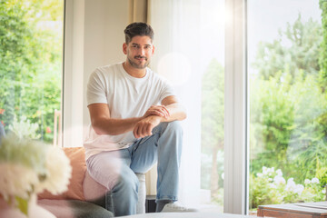 Confident man wearing casual clothes and smiling while relaxing at home