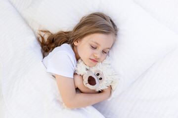 cute baby girl sleeping sweetly on the bed on a white cotton pillow under the blanket and hugging a...