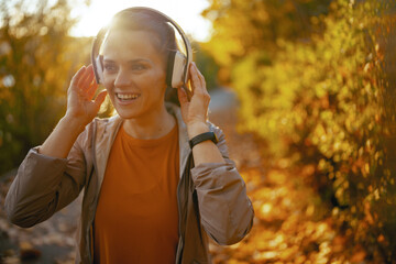 happy woman in fitness clothes in park listening to music