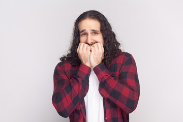 Portrait of bearded man in checkered red shirt looks nervously, bites finger nails, watches moving...