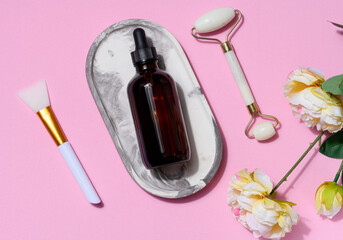 Brown glass bottle with a pipette, a green stone hand massager for cosmetic procedures on a pink background, top view