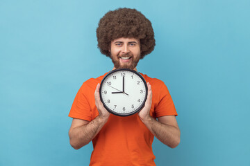 Portrait of satisfied delighted man with Afro hairstyle wearing orange T-shirt holding in hands big...