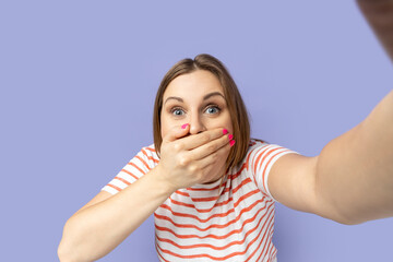 Portrait of amazed astonished woman in striped T-shirt taking selfie picture, covering her mouth...
