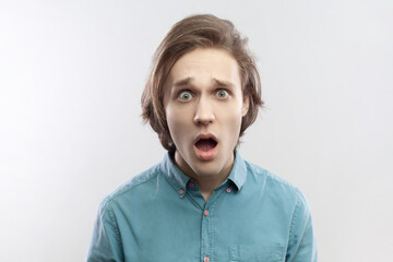 Obraz na płótnie Canvas Portrait of shocked amazed astonished young man looking at camera with big eyes and open mouth, sees something amazing, wearing blue shirt. Indoor studio shot isolated on gray background.
