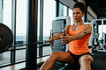 Fototapeta na wymiar Strong and confident sportswoman athlete working out in fitness gym and doing cable row exercise. Strong and healthy concept. Focus on performance