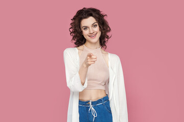 Portrait of satisfied smiling attractive woman with curly hairstyle in casual style outfit pointing...