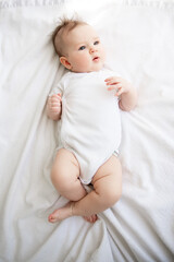 The baby lies on his back in a white bed in the morning.