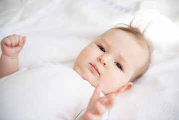 Charming baby on a white bed in the bedroom.