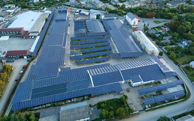 Aerial view of solar power plant with blue photovoltaic panels mounted on industrial building roof...