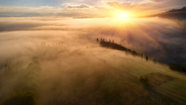 Fog spreads over the mountains at dawn. The sun rises on the horizon. Carpathians in the morning. Aerial drone view. © Ryzhkov Oleksandr