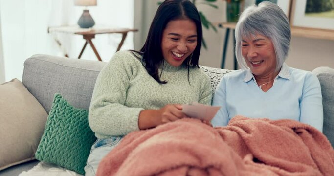 Talking, happy and daughter with mother and pictures on the living room sofa, laughing and bonding. Happy, family and Asian woman speaking to an elderly mom about a memory with a photo on the couch