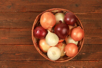 Various varieties of onions in a basket on a wooden background, autumn harvest concept, red, white and golden onions for breeding in agriculture, selective focus