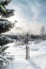 Cross and the winter snowy landscape at Filipova Hut, Sumava national park, sun shining behind the trees