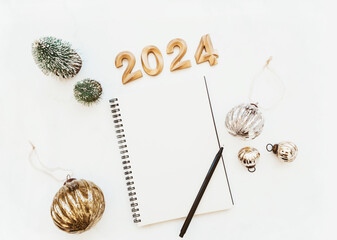 Flat lay of blank notebook sheet with copy space, numbers 2024, christmas decoration, christmas balls on white marble background.