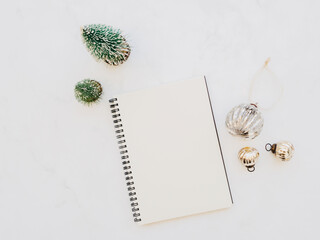 Flat lay of blank notebook sheet with copy space, christmas decoration, christmas balls on white marble background.