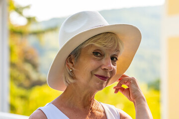 Portrait of a beautiful woman 60-70 years old in a felt white hat on a blurred background of...