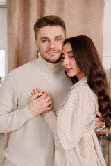 Happy young couple in love is hugging gentle and smiling together celebrating Valentine's day at cozy Scandinavian style home. Man and woman enjoying spending time together, relaxing on date.