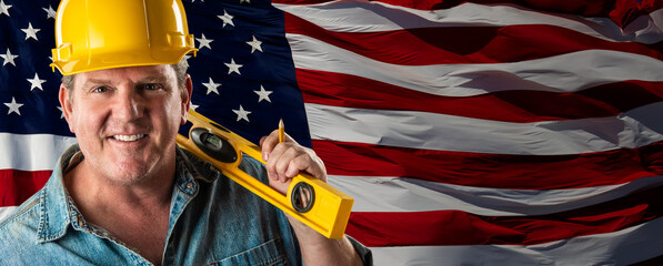 Male Contractor Wearing Blank Yellow Hardhat Over Waving American Flag Background Banner.