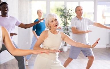 Fototapeta premium Group of multinational sports aged people rehearsing modern dance in dance hall