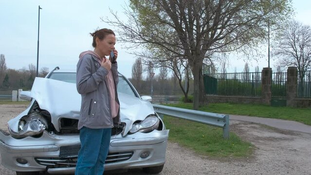 Female call emergency services by smashed car. A view of stressed woman driver call somebody by the crashed car in the street.