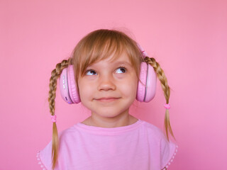 Little cute cheerful girl listening to music, audiobooks, studies languages in wireless pink...