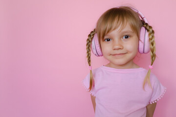 Little cute cheerful girl listening to music, audiobooks, studies languages in wireless pink...