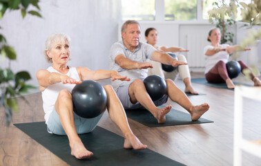 Elderly woman doing pilates with soft ball in group on mat in fitness studio