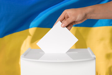 Fototapeta premium Man putting his vote into ballot box against national flag of Ukraine, closeup