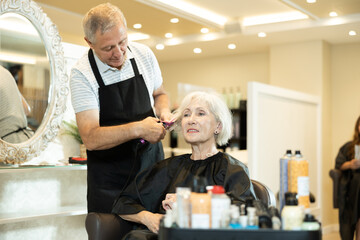 Experienced focused hairdresser using curling wands to create waves and add volume to silver hair...