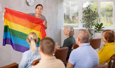 Young female professor showing flag of lgbt pride to elderly students