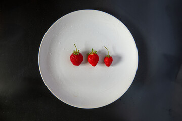 Fresas en un plato blanco vistas directamente desde arriba, sobre un fondo negro