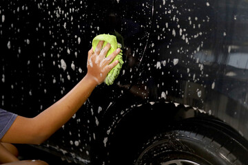 Worker washes black car with microfiber cloth at car wash