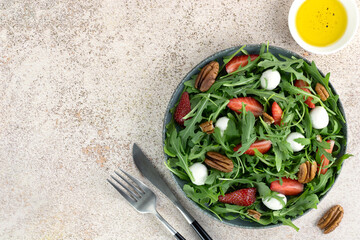 Green salad with strawberries, mozzarella balls, arugula and pecans on pink background. Top view. Copy space.