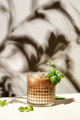 Mint White Russian cocktail drink with vodka, coffee liqueur, mint schnapps, cream and ice cubes on beige background, hard light, shadow pattern