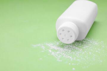 Bottle and scattered dusting powder on light green background, space for text. Baby cosmetic product