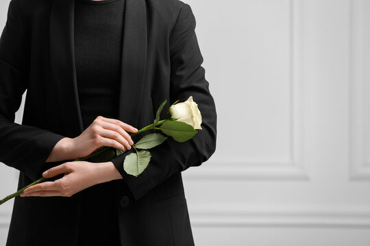 Woman with rose flower near white wall, closeup and space for text. Funeral ceremony