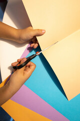 Vertical photography of a children cutting some color cupboards getting ready to be back to school. Kid making crafts with some papers and scissors.