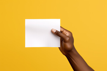 A human hand holding a blank sheet of white paper or card isolated on yellow background