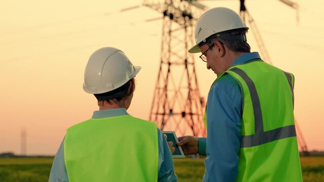 Electrical engineers work on digital tablet near power poles. Industry concept. Engineers builders, tablet computer, power unit tower with electricity. Business people. Supply electric energy consumer