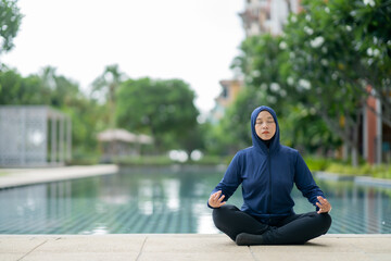 Athletic Asian Muslim Sports Woman Wearing Hijab and Sportswear relaxes in yoga pose in green nature park, Healthy and lifestyle concept, Muslim yoga concept.