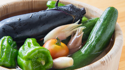 夏野菜イメージ・木桶に水を入れて野菜をつける｜きゅうり・なす・ピーマン・ミニトマト・オクラ・ミョウガ © aomas