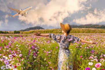 Beautiful autumn background. A woman in a floral dress and hat stands in a field of cosmos, arms wide open, watching an airplane take off. 
 - Powered by Adobe