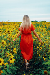 A young woman in a red dress walks through a field of sunflowers.