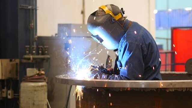 Metal welder working with arc welding machine to weld steel at factory