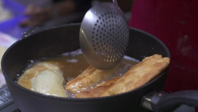 Meat roll and samosa deep fried and stirred in oil hot oil, filmed as close up in handheld style