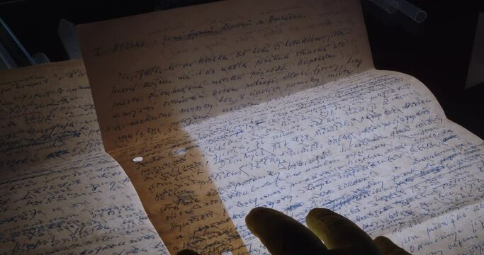 Hands of a forensic specialist wearing protective gloves examine handwritten letters on a backlit table